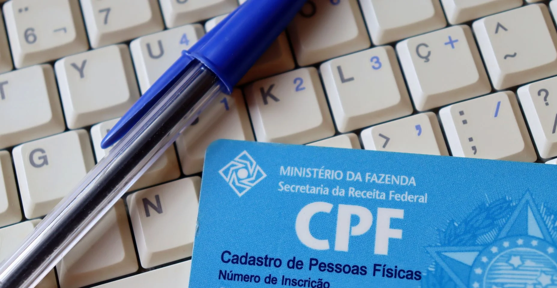 (CPF - Cadastro de Pessoas Físicas) e caneta em cima do computador. O número do CPF é a identificação do cadastro de pessoa física brasileira.