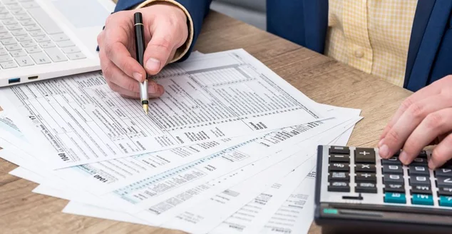 Empresário trabalha com formulário de imposto 1040, laptop e calculadora