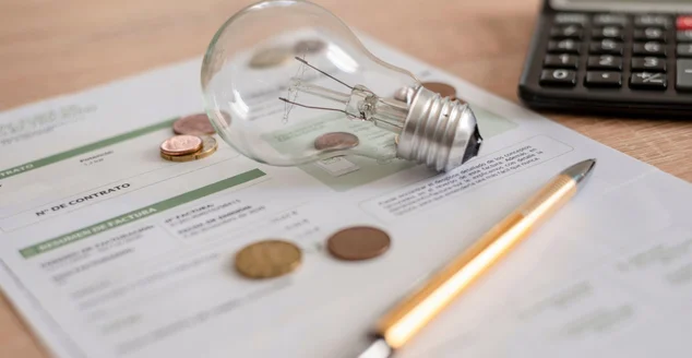 Conta de eletricidade com lâmpada, diversas moedas, calculadora e caneta em cima da mesa. Conceito de preços de eletricidade e pagamentos de impostos.