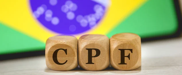 A sigla CPF para Registro de Pessoa Física em português brasileiro escrita em dados de madeira. Ao fundo, a bandeira do Brasil na tela de um celular.