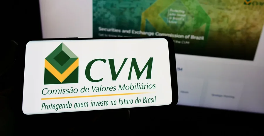 Pessoa segurando smartphone com logotipo da Comissão de Valores Mobiliários (CVM) brasileira na tela em frente ao site. Concentre-se na tela do telefone.