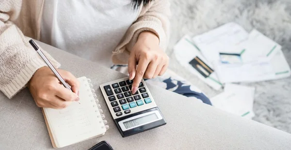 Mulher escrevendo uma lista de dívida em notebook calculando suas despesas com calculadora