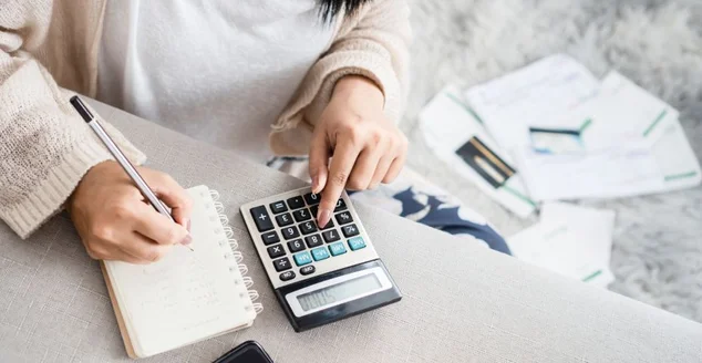 Mulher escrevendo uma lista de dívida em notebook calculando suas despesas com calculadora