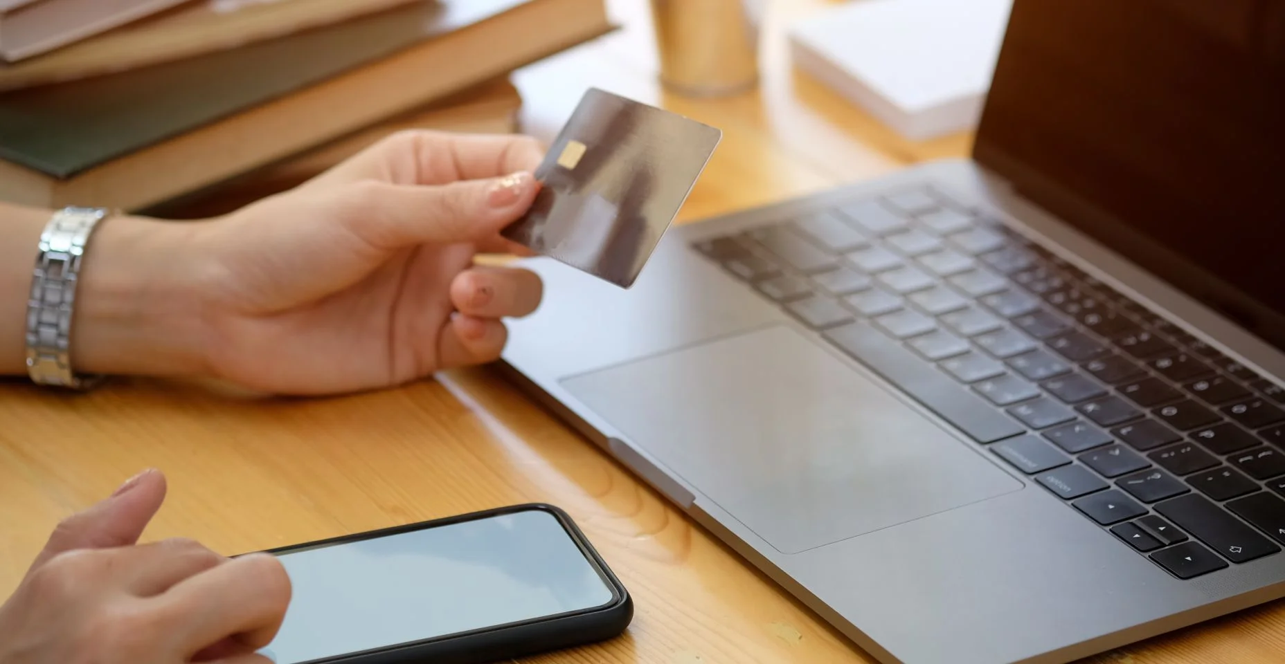 Cortada de tiro de mão feminina segurando plástico de cartão de crédito e usando telefone inteligente na mesa no escritório. Conceito de pagamento de compras online.