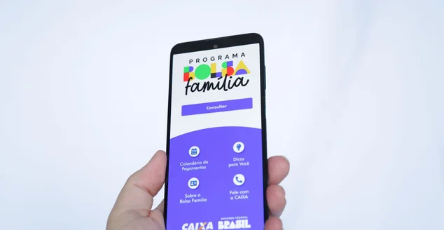 Mão masculina segurando um smartphone com o aplicativo Bolsa Familia do governo.