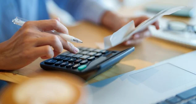 Mulher sentada à mesa fazendo plano financeiro e orçamento com calculadora e laptop