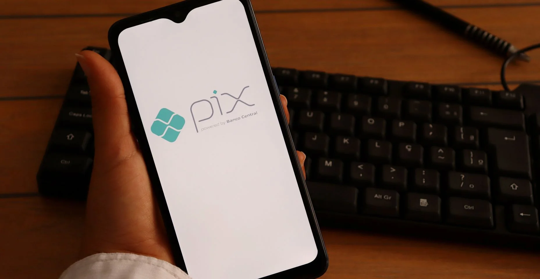Mão de uma mulher segurando smartphone com logotipo Pix na tela, na mesa do escritório. Pix Brasil é um sistema de pagamento instantâneo.