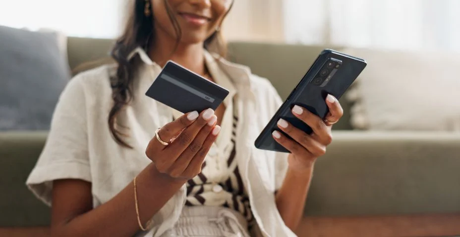 Mulher feliz, mãos e telefone com cartão de crédito para compras online, pagamento ou transação na sala de estar em casa. Closeup da pessoa feminina ou comprador no smartphone móvel com débito para comércio eletrônico