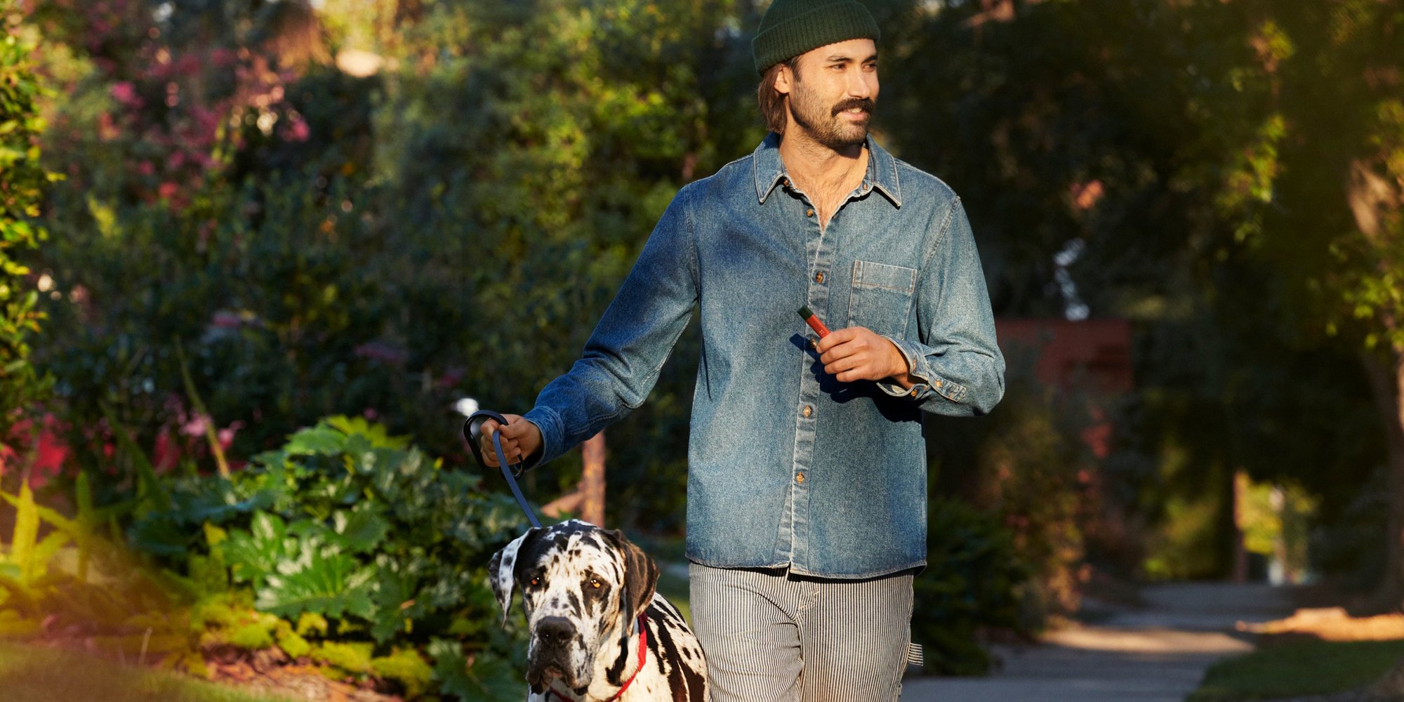 A guy with a beanie and mustache out walking his Dalmatian using a Pax Era