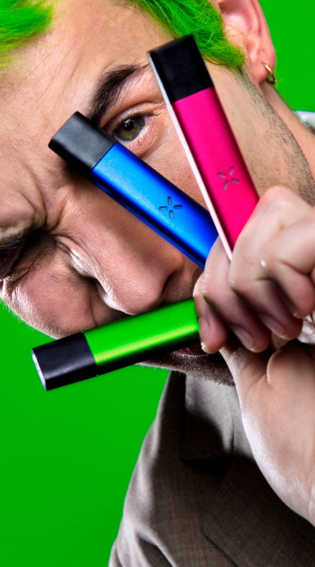 Guy with green hair holding four Pax Era vape pens between his fingers