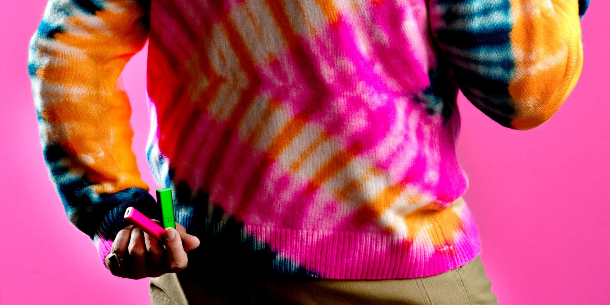 Person holding a couple of PAX Era vaporizers behind their back with a tie dyed sweater