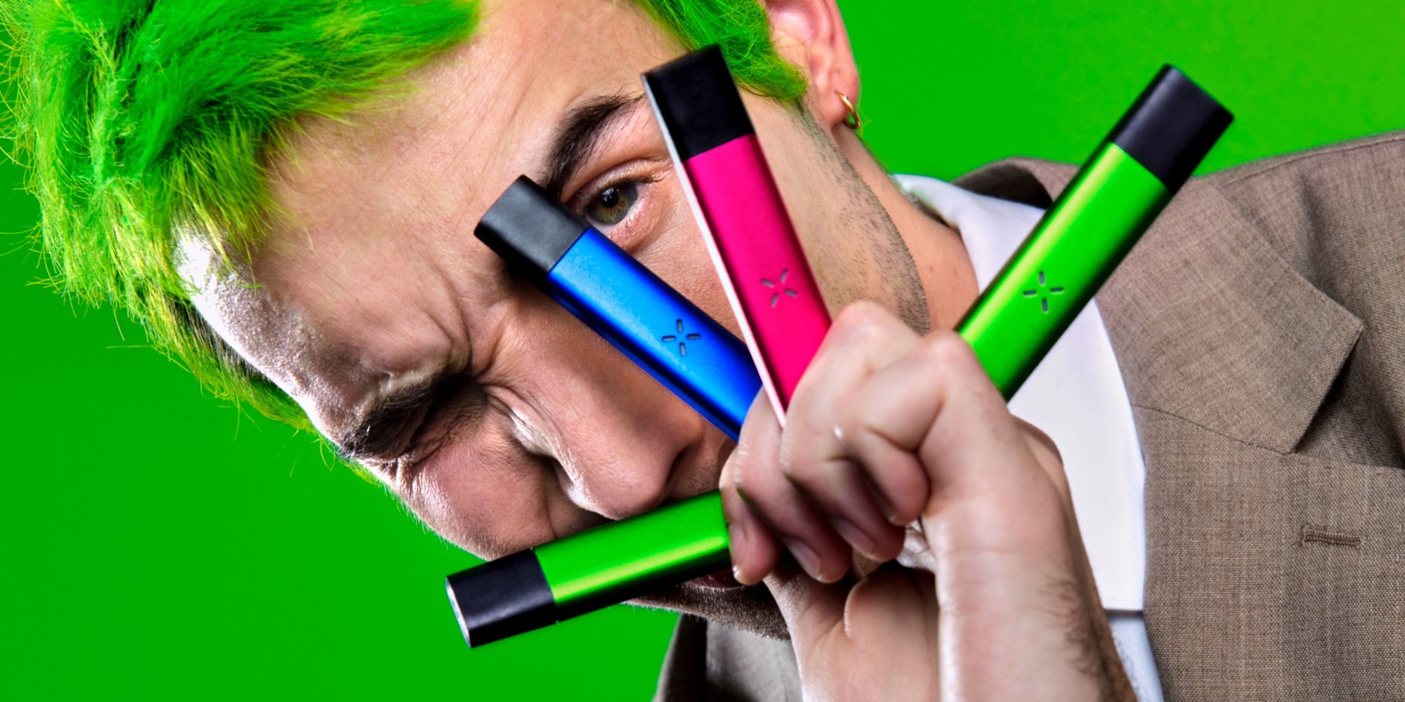 Guy with green hair holding four Pax Era vape pens between his fingers