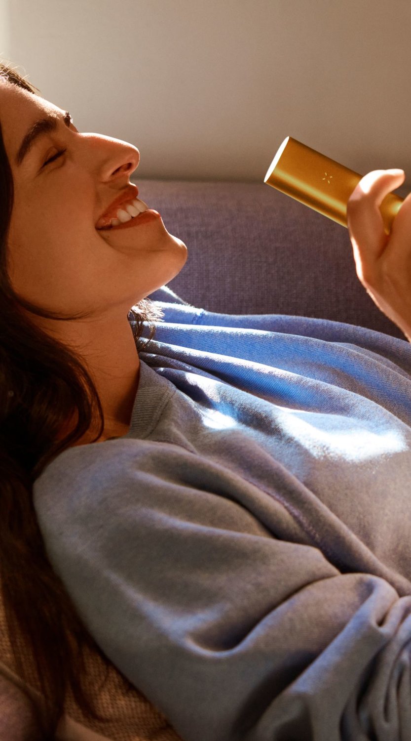 Woman relaxing on a couch enjoying a PAX vaporizer