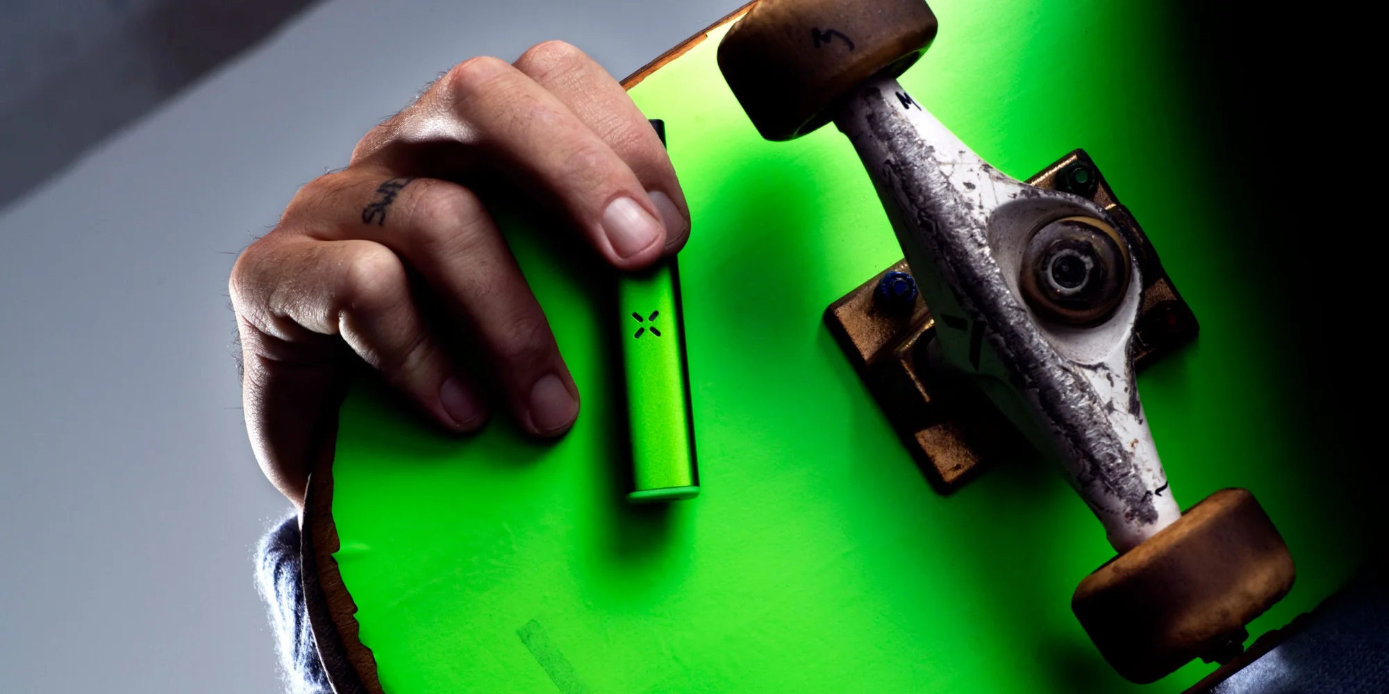 Holding a green skateboard with a pax era vaporizer