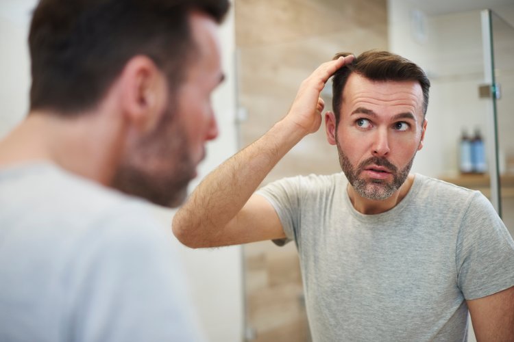 Middle aged man looking in the mirror touching his thinning hair.