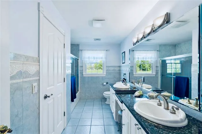 Finished bathroom with double sinks, a granite counter, and tiled walls