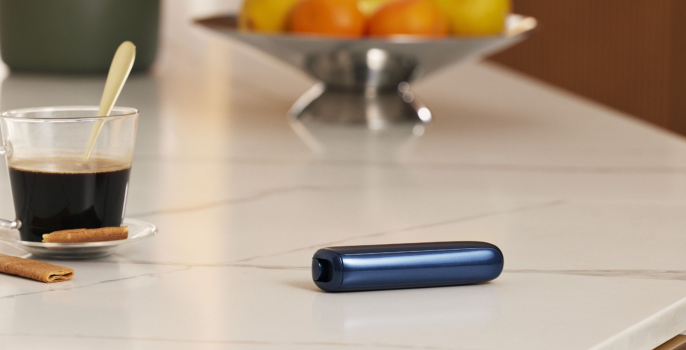 Ploom AURA Lunar Silver na stolu s nekoliko prednjih poklopaca.