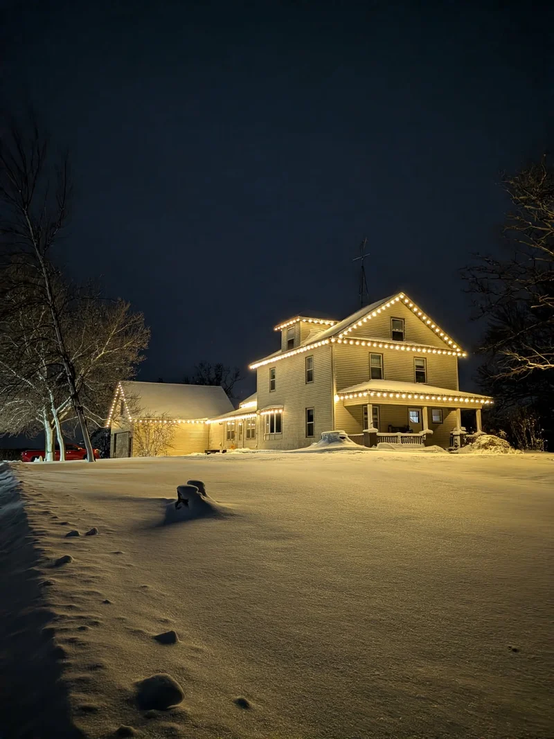 Snowy home with warm white Christmas lights illuminating the roofline
