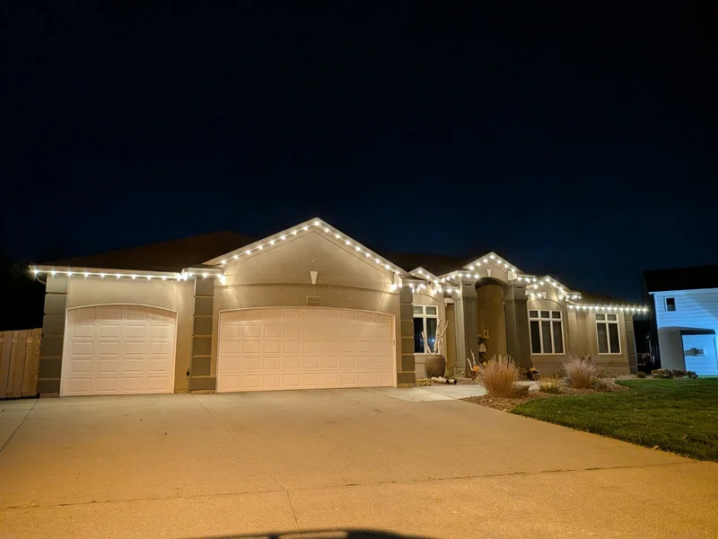 Brightly lit home with warm white Christmas lights across the roof and garage