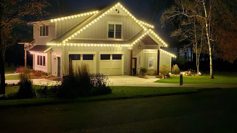 Two-story home with warm white Christmas lights outlining the roof and entry