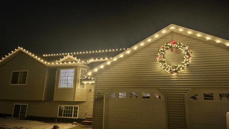 Large home with warm white roofline lights and a decorated holiday wreath
