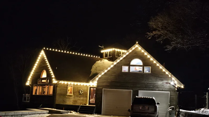Cabin-style home with warm white Christmas lights along the roofline