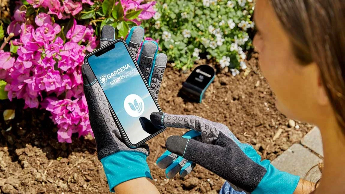 Frau verwendet GARDENA smart system App am Blumenbeet