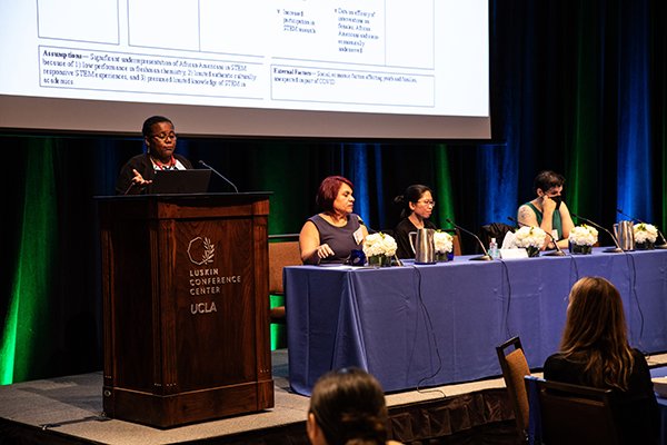 Oluwatoyin Asojo, PhD stands at the podium presenting while the other three panelists are seated at a table.