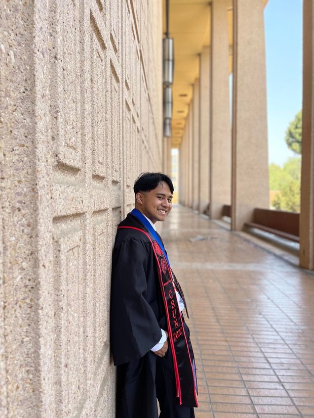 Raphael Zambrano smiling proudly wearing his graduation robe and stole.