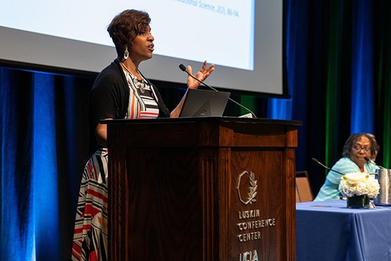 Angela Byars-Winston, PhD speaking on stage at a podium.