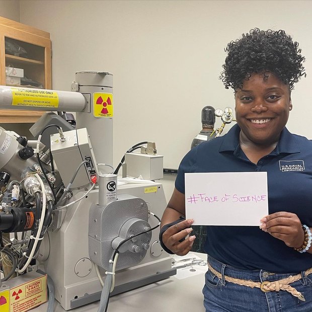 Treva Brown, PhD standing in a lab holding a sign with #FaceOfScience written on it.