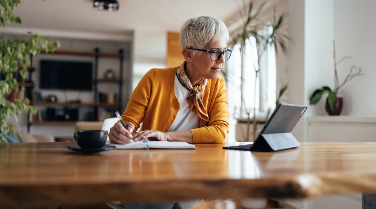 Woman writing notes while using a tablet at home