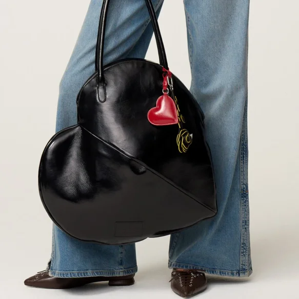 Vrouw in gestreept overhemd en jeans met grote zwarte leren tas met rood hartje hanger.