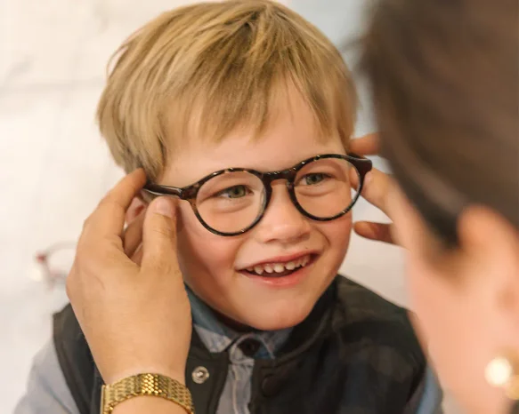 Lachende jongen krijgt een donker rond kindermontuur opgezet door een opticien in de winkel.