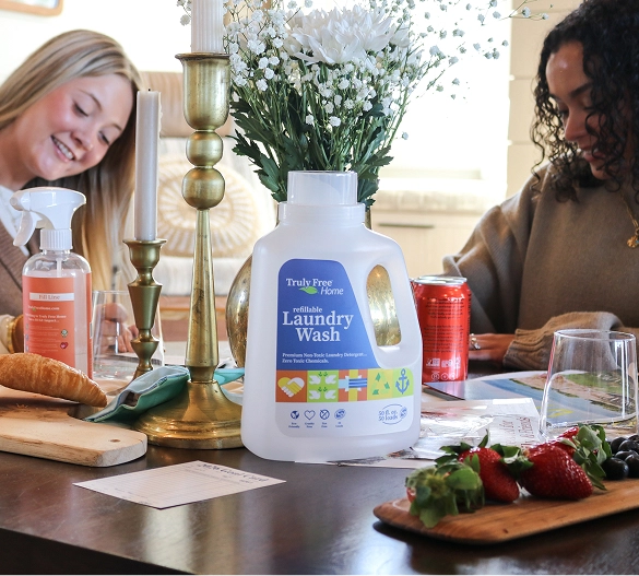 Truly Free Laundry Wash and refill pouch in a laundry room, with a woman and baby in the background.