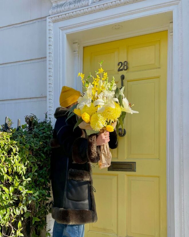 A person knocking on a door with a large bouquet of yellow flowers