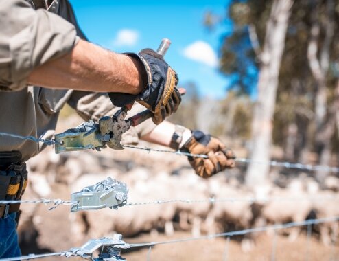 Man's arms building barb wire fence