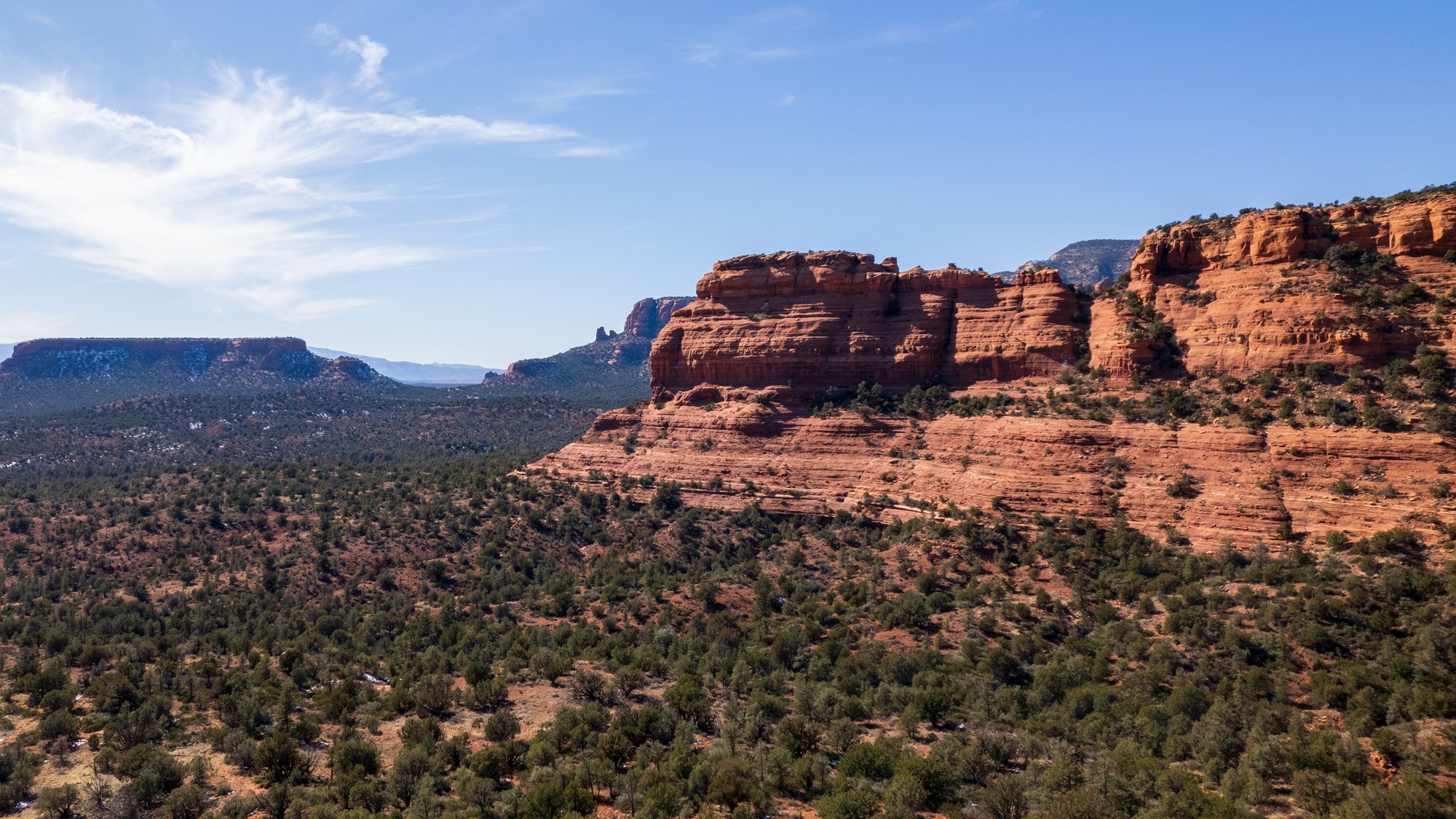 A picturesque Arizona desert scene with a touch of greenery amidst the arid landscape. In the foreground, majestic land masses, their slopes adorned with sparse vegetation, rise against the clear blue sky. 