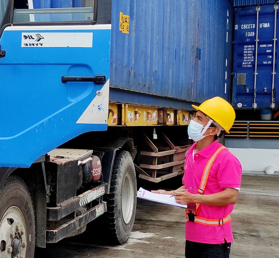 Close-up of a Karzo Employee in a Karzo Uniform, holding paper, next to a blue shipping container.