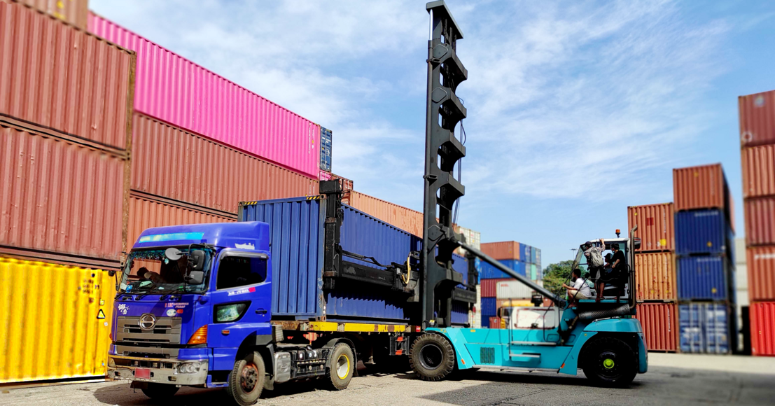 Blue truck with containers being loaded by a yellow forklift in a shipping yard, representing logistics and cargo transport.