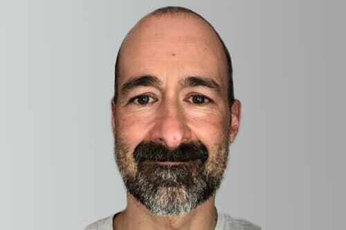 Head of Antibody Technology, Bijan Etemad-Gilbertson, Phd, with a bald head and a salt-and-pepper beard smiling slightly at the camera.