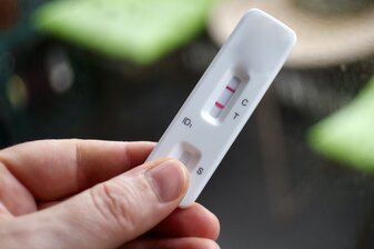 Hand holding rapid diagnostic test cassette displaying positive result for detection