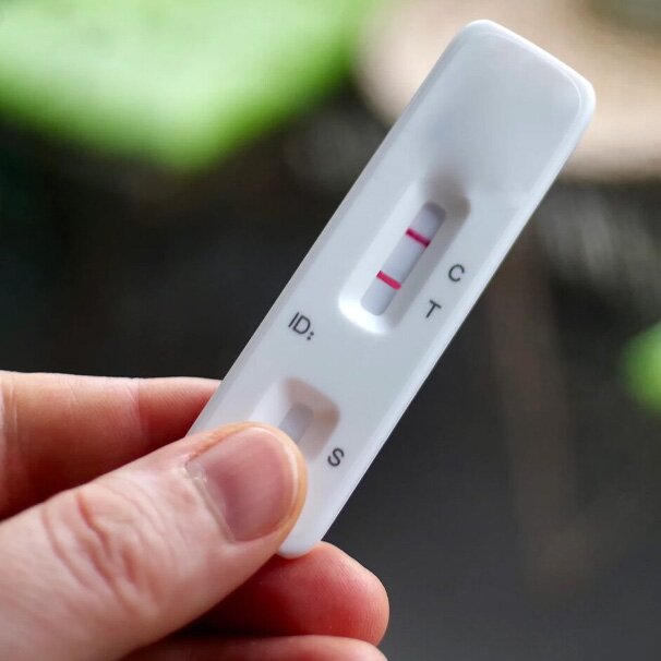 Hand holding a rapid diagnostic test cassette showing two lines.