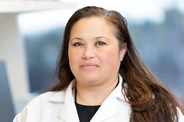 Scientist in a white lab coat with long hair posing in a laboratory setting