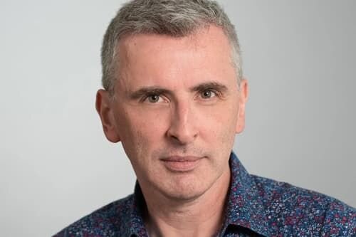 Portrait of a middle-aged man with short gray hair, wearing a patterned shirt, looking directly at the camera - Keogh