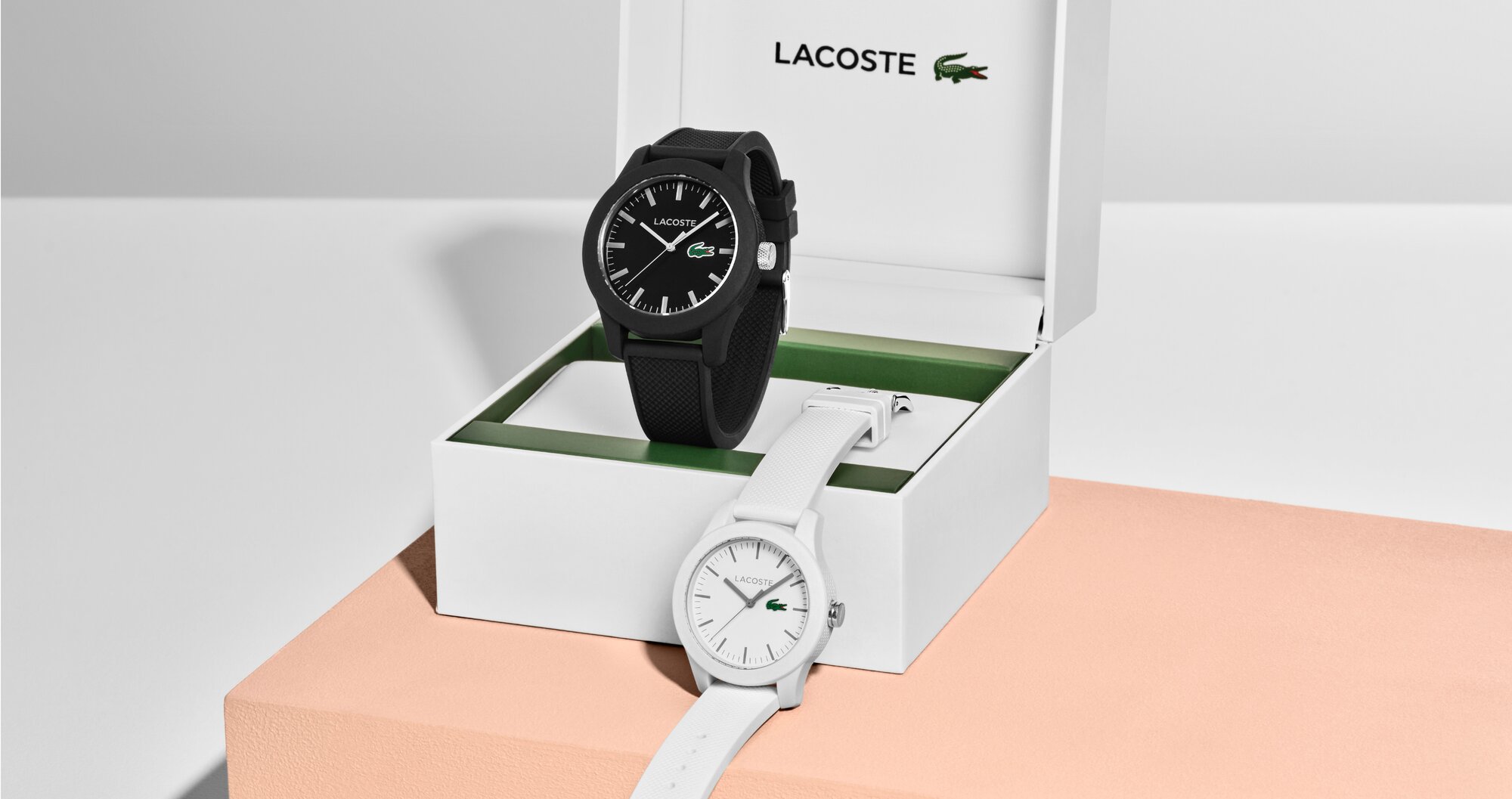 Lacoste 12.12 men's black strap and women's white strap displayed with the Lacoste gift box