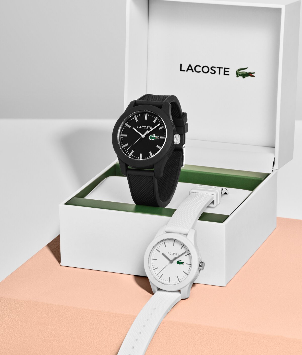 Lacoste 12.12 men's black strap and women's white strap displayed with the Lacoste gift box