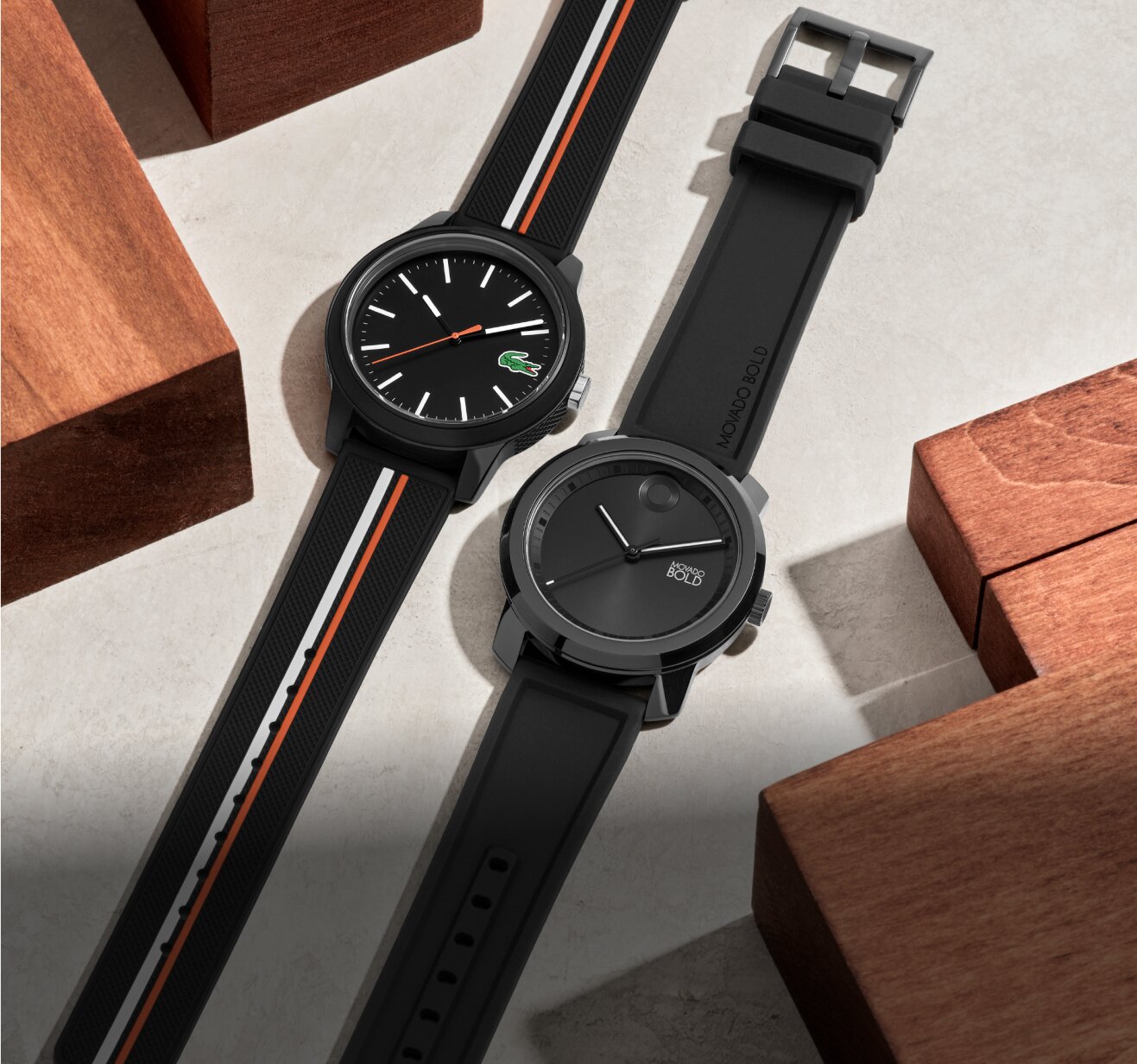 Movado Trend Propel with black strap and Lacoste 12.12 with black strap laying flat showcasing day to night black watches