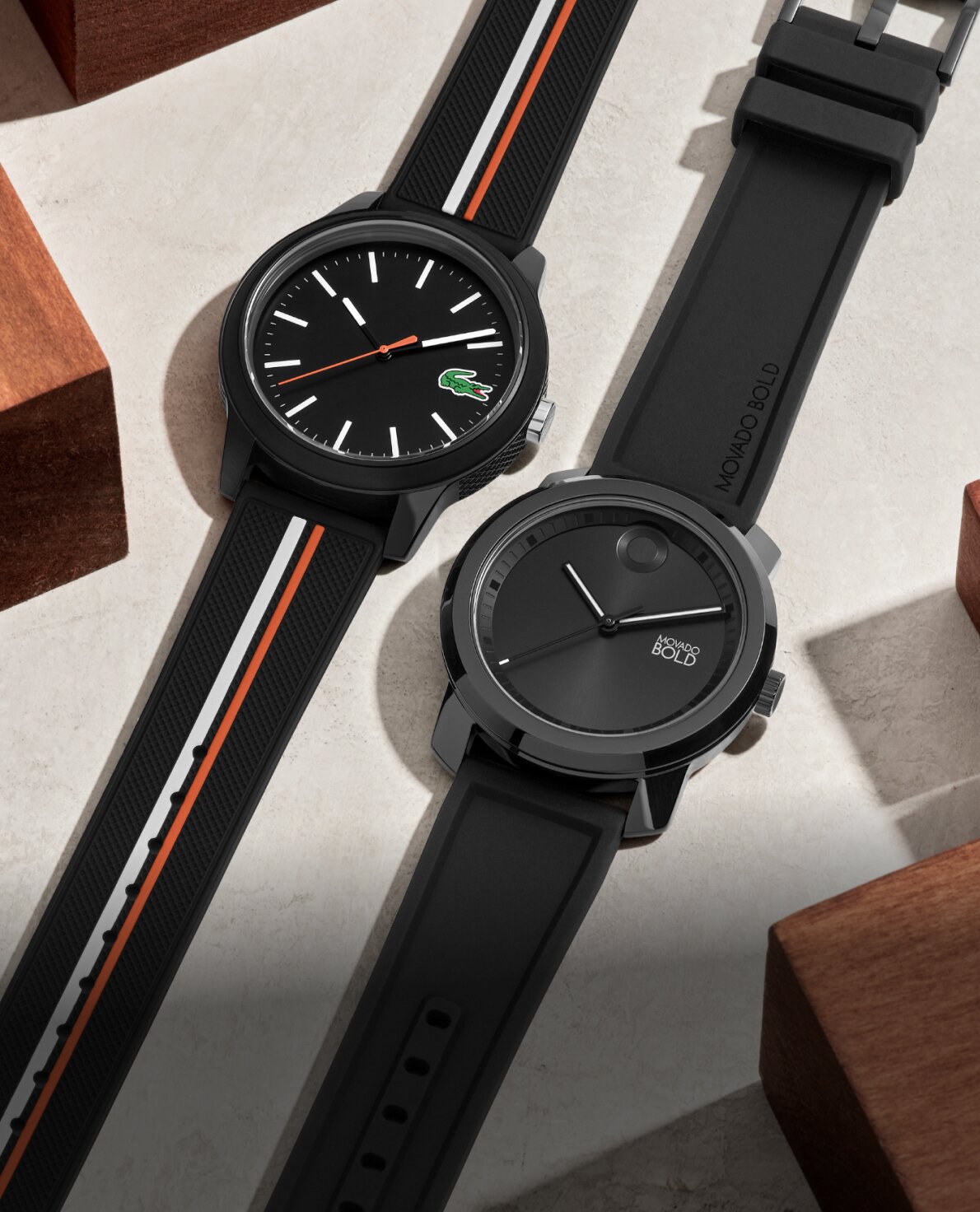 Movado Trend Propel with black strap and Lacoste 12.12 with black strap laying flat showcasing day to night black watches