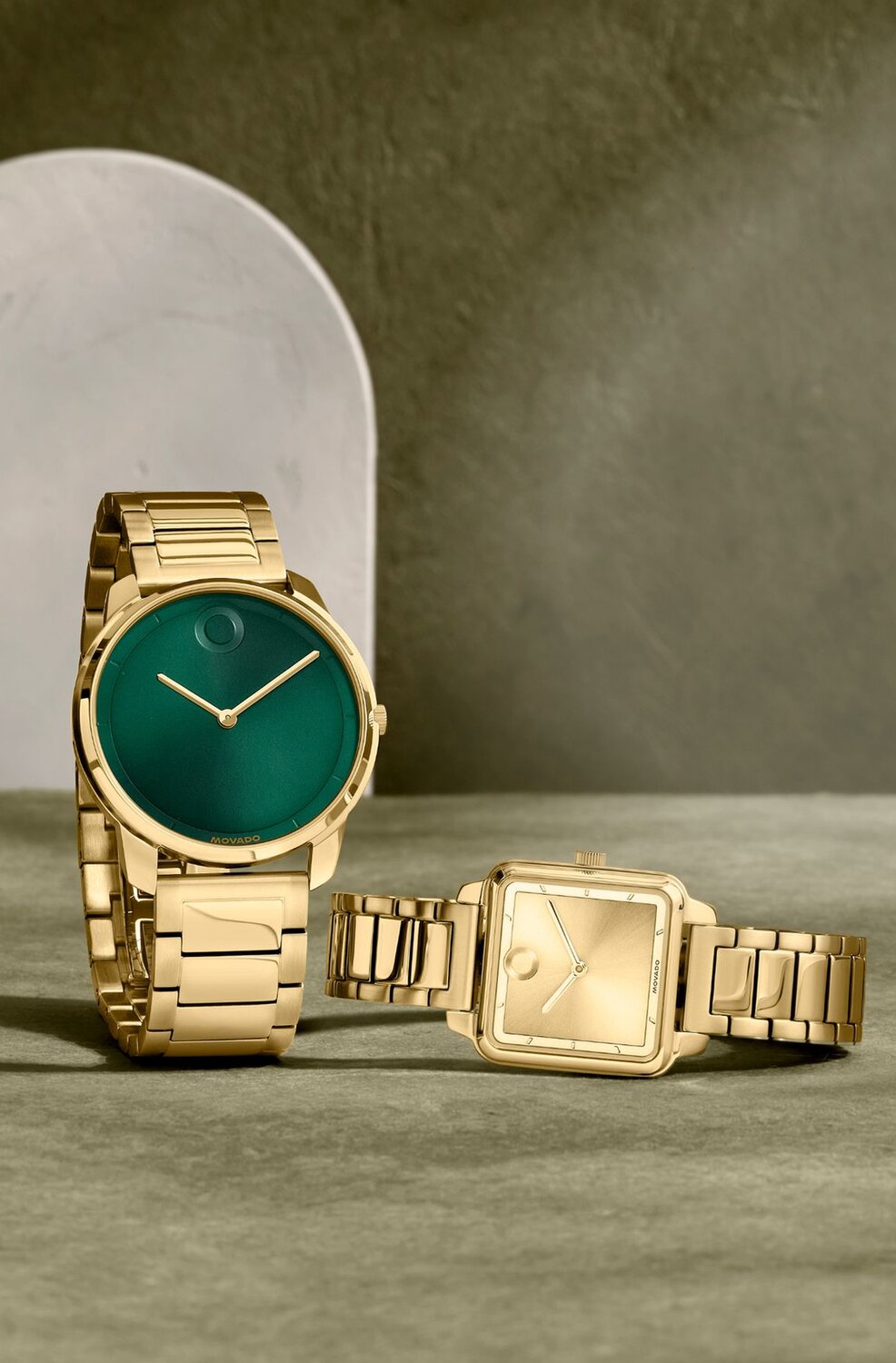 Movado Trend men’s green-dial gold watch beside women’s gold watch with shaped dial